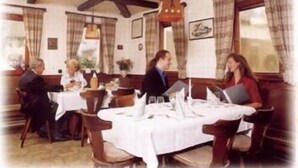 Un restaurante con vigas de madera, manteles blancos y cortinas a cuadros.