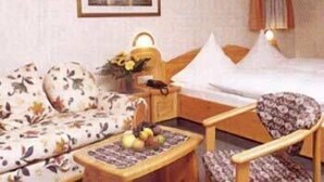 Habitación de hotel con cama, sofá, sillón y una mesita con fruta.