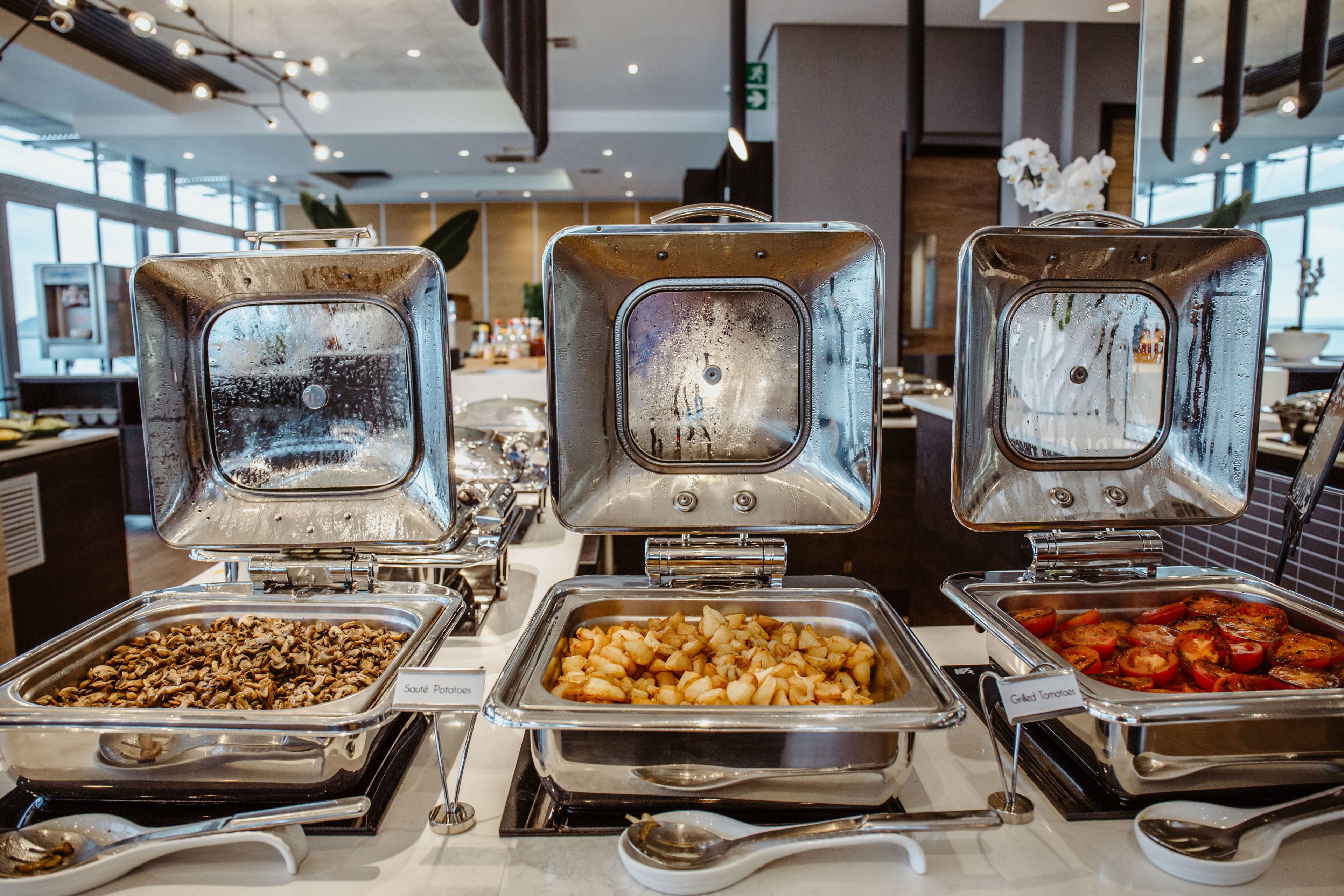A buffet with various food options including sautéed potatoes, sautéed mushrooms, and grilled tomatoes.