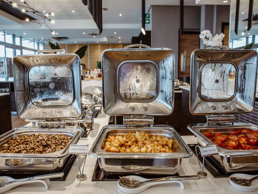 A buffet with various food options including sautéed potatoes, sautéed mushrooms, and grilled tomatoes.