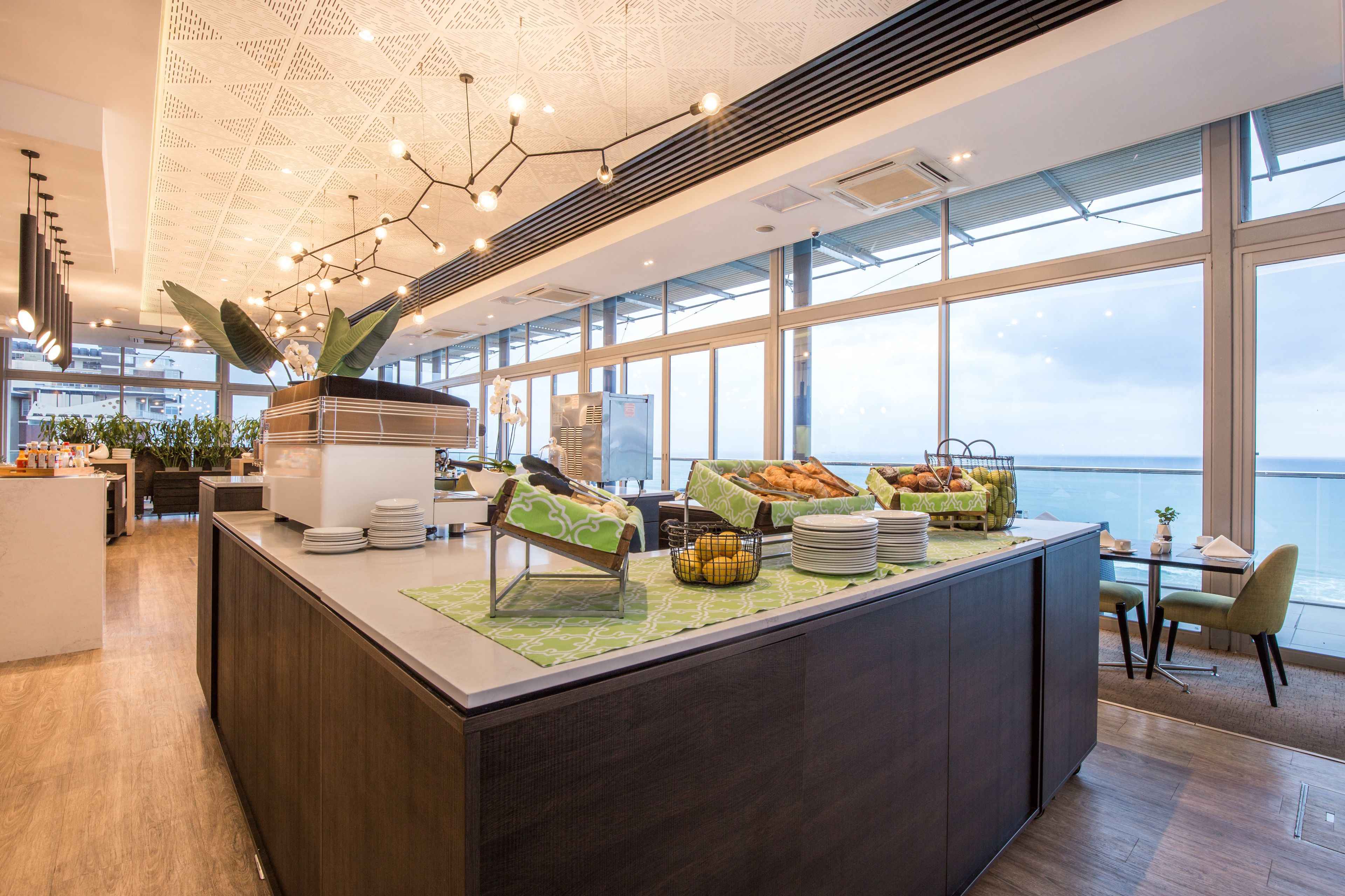 Una barra de desayuno moderna con vistas al mar, que ofrece un bufé con frutas y pastelería.