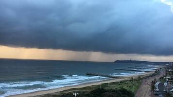 Vista costera con playa, paseo marítimo y cielo tormentoso.