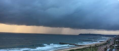 A coastal view with a beach, promenade, and a stormy sky.