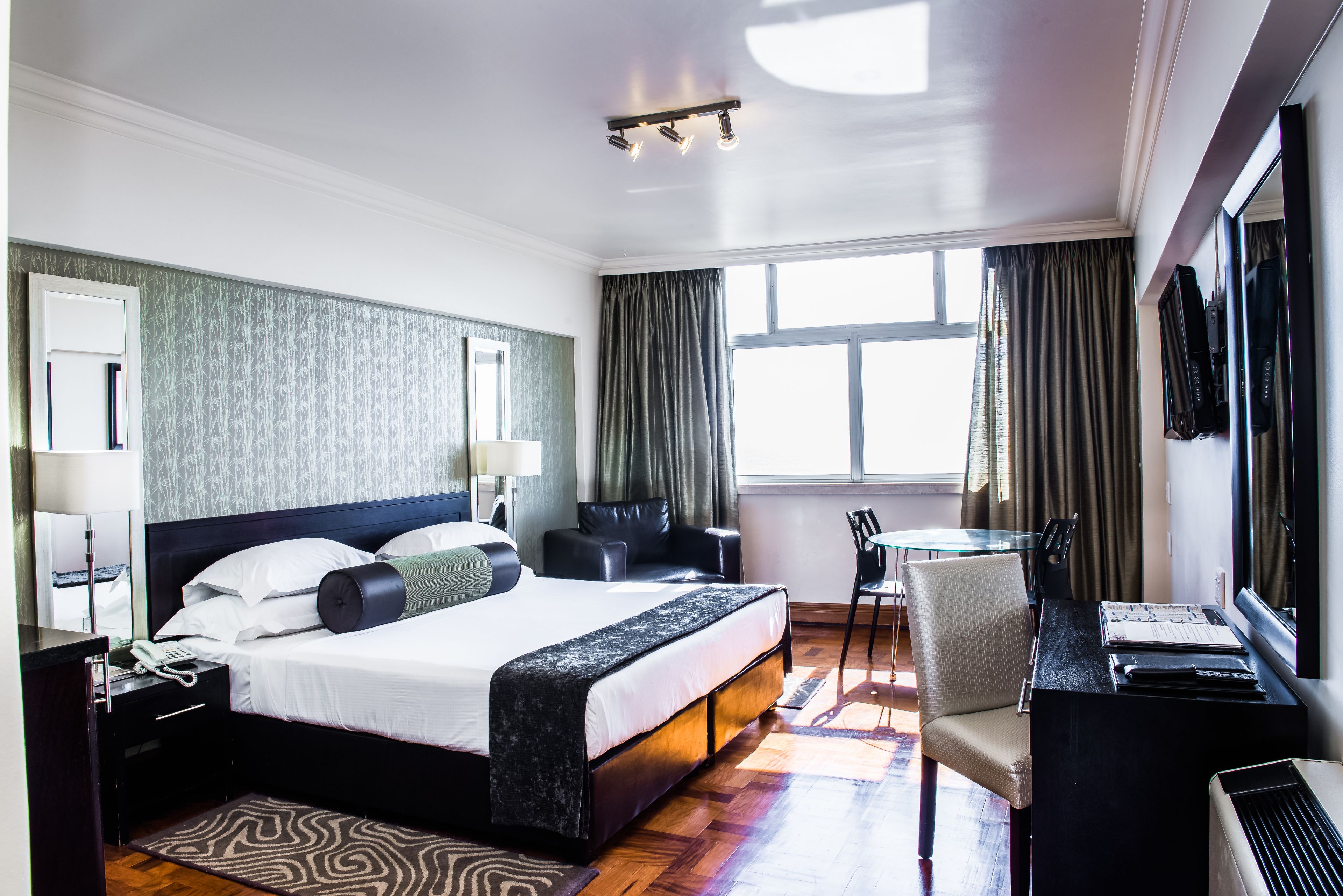 Habitación de hotel con una cama grande, un escritorio con silla, televisor y ventana con cortinas.