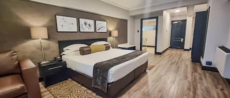 A hotel room with a large bed, bedside tables, a lamp, a chair, and a patterned rug.