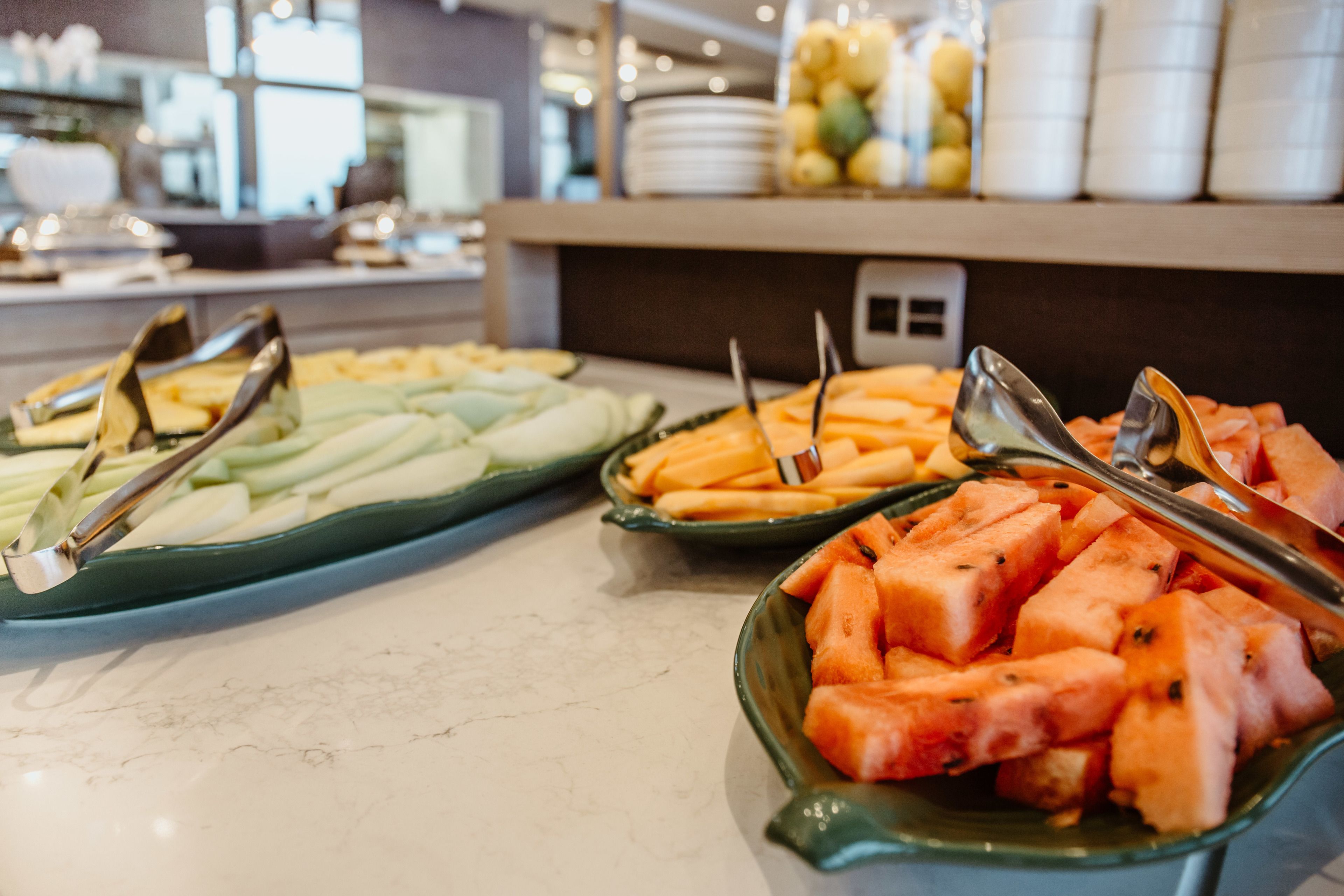 A buffet with various fruits and vegetables, including sliced cucumbers, carrots, and watermelon, arranged on a marble countertop.