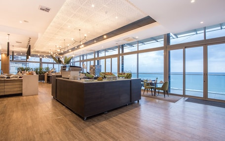 A modern kitchen with a large island, a view of the sea, and a high ceiling with geometric patterns.