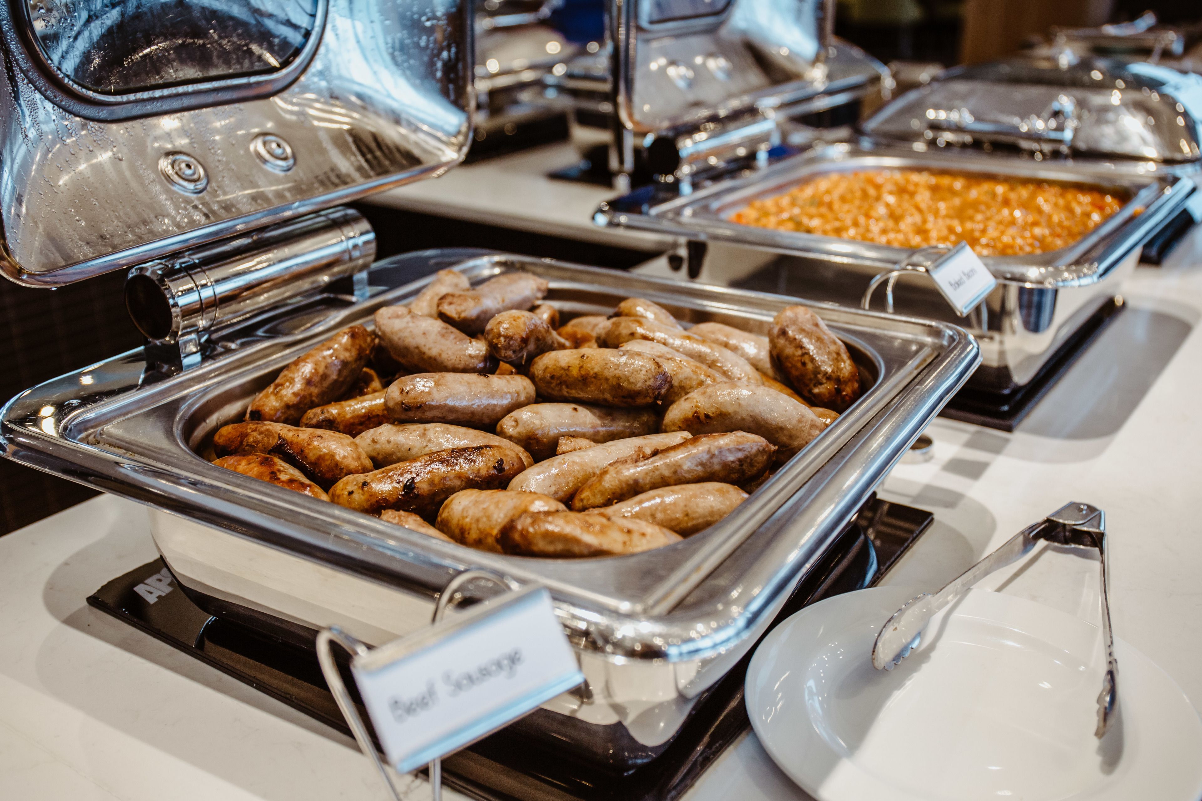 A buffet with various food items, including sausages and beans.