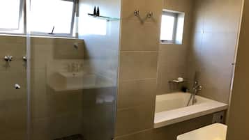 A modern bathroom with a glass shower enclosure, a white bathtub, and a small window above the sink.