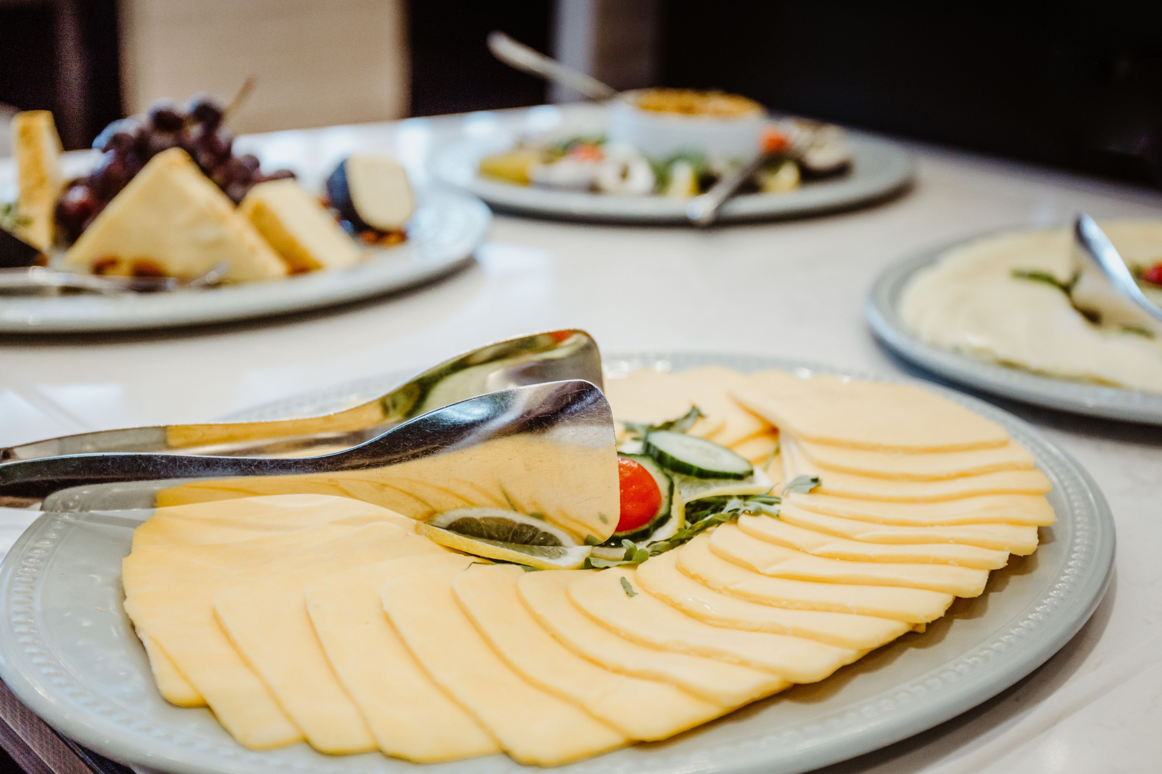 Una mesa de buffet con alimentos ordenados, entre ellos queso en rodajas y una ensalada.