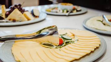 Una mesa de buffet con alimentos ordenados, entre ellos queso en rodajas y una ensalada.