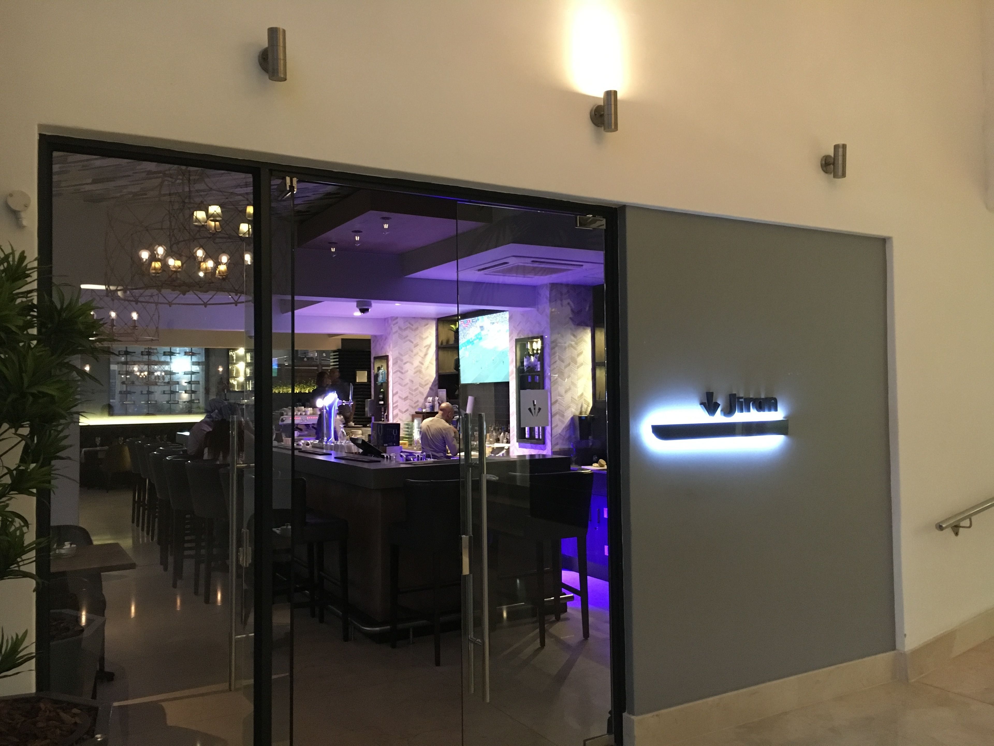 Un área de bar moderna con mampara de vidrio, taburetes y luz ambiental.
