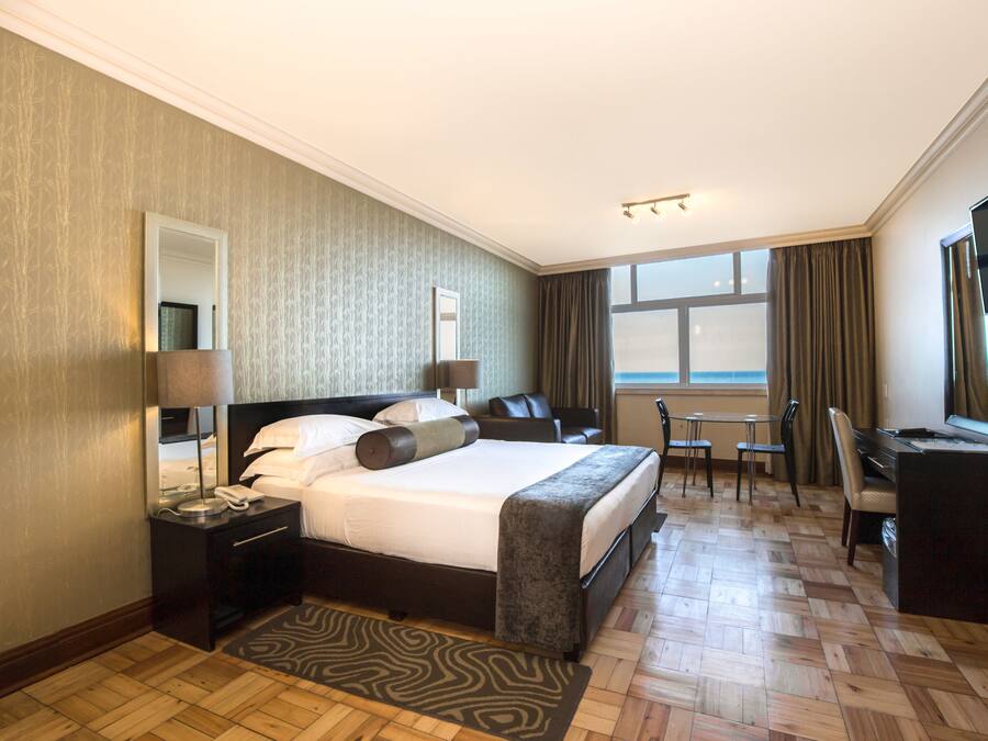 Une chambre d’hôtel avec un grand lit, un bureau, une chaise, une télévision et une fenêtre avec des rideaux.