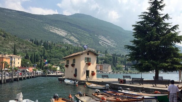 A marina with boats docked, a small building, and a mountainous backdrop. - Al Caminetto (Nago-Torbole)