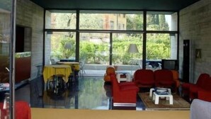 A modern room with large windows, a dining table, and red chairs. - Al Caminetto (Nago-Torbole)