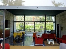 A modern room with large windows, a dining table, and red chairs.