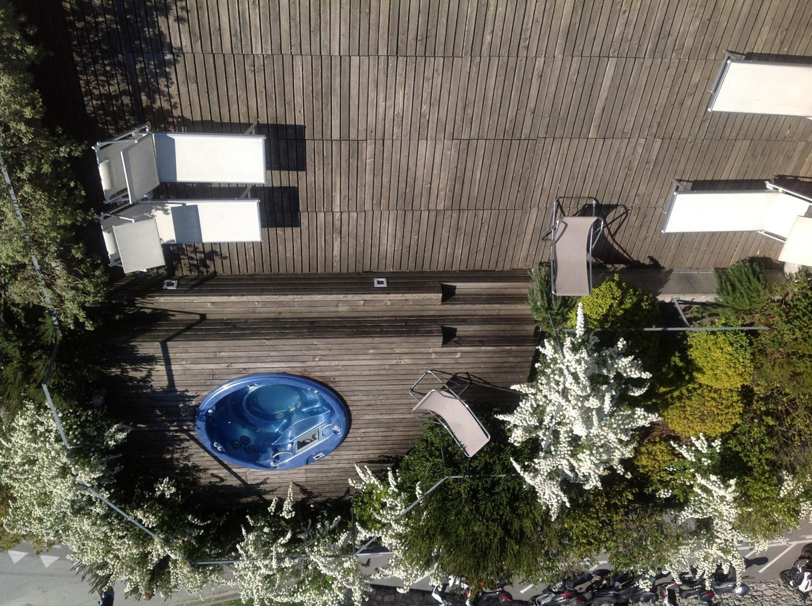An aerial view of a rooftop with a swimming pool, surrounded by trees and a wooden deck.