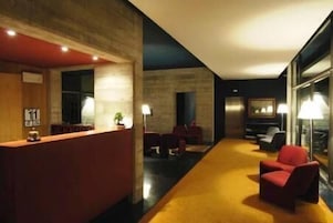 Um hall de hotel moderno com balcão de recepção, área de estar e uma grande janela.