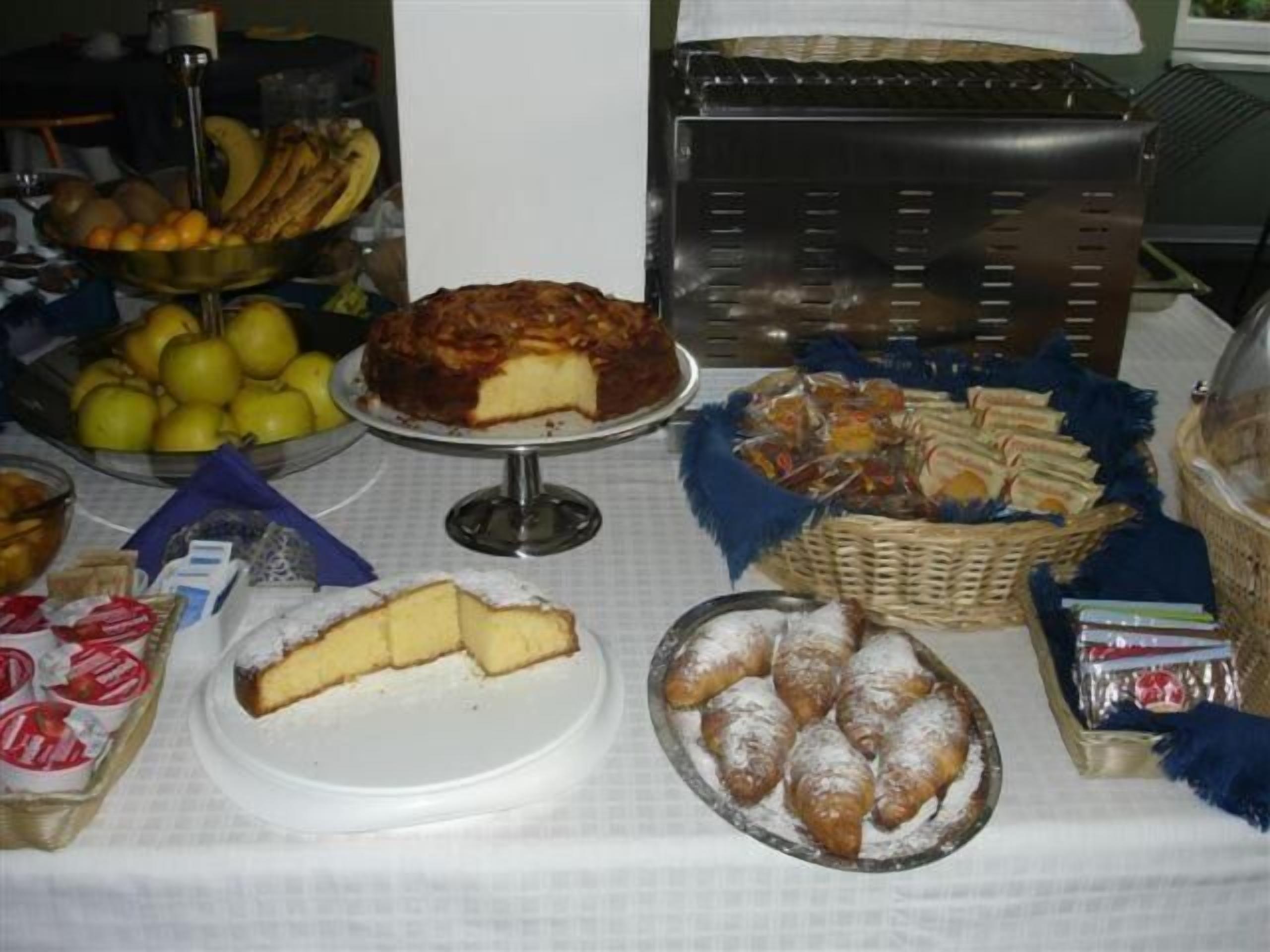 Una mesa de buffet con diferentes tipos de comida, incluyendo un pastel, productos de pastelería, frutas y salsas.