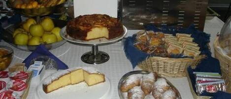 Una mesa de buffet con diferentes tipos de comida, incluyendo un pastel, productos de pastelería, frutas y salsas.