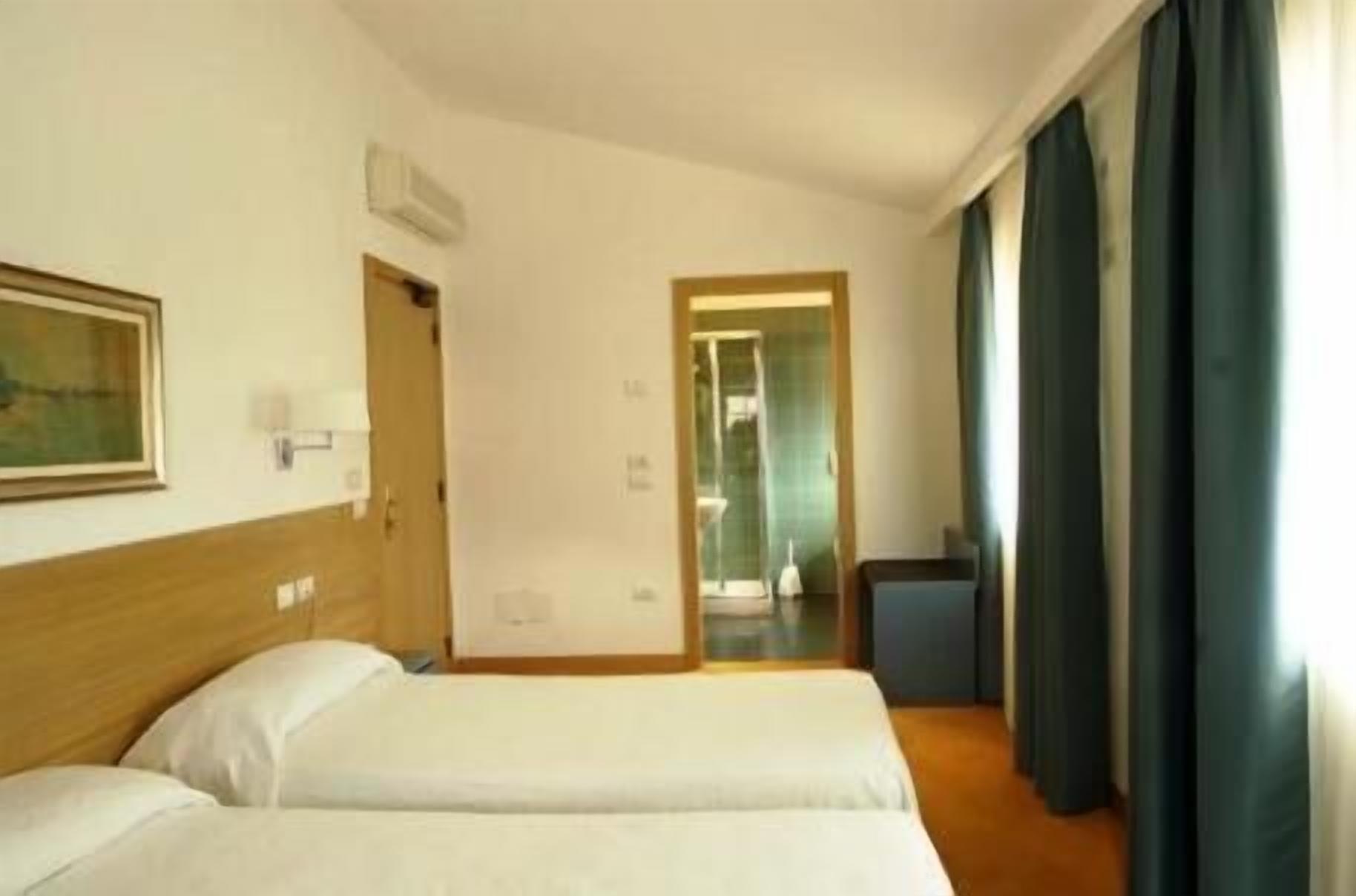 A hotel room with two beds, a wooden headboard, a painting on the wall, and a view of the bathroom through a door.