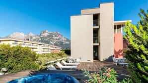 A modern building with a pool area, surrounded by greenery and mountains in the background. - Al Caminetto (Nago-Torbole)