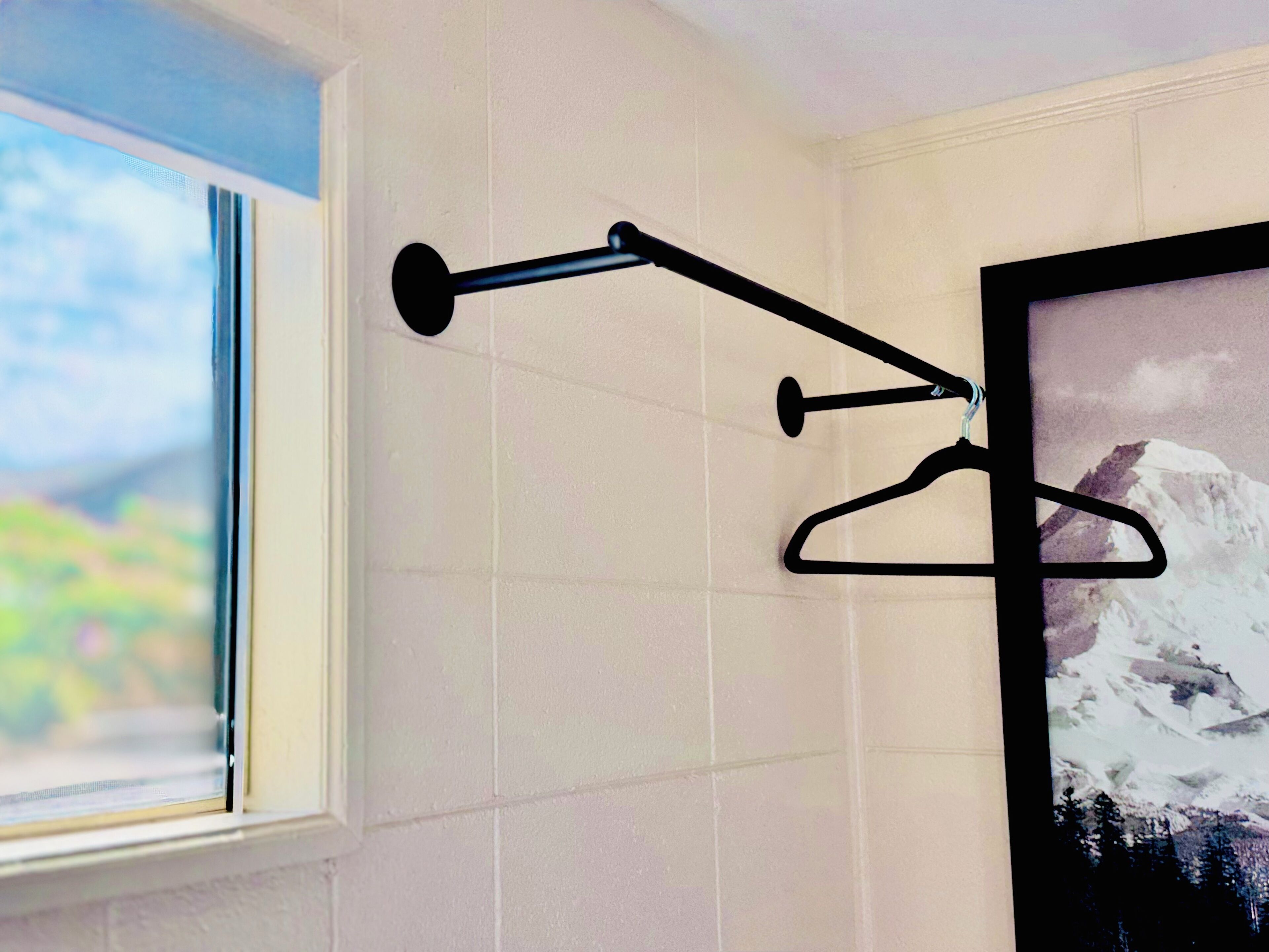 A bathroom with white tiled walls, a window with a view of greenery, and a black towel rack with two towels.