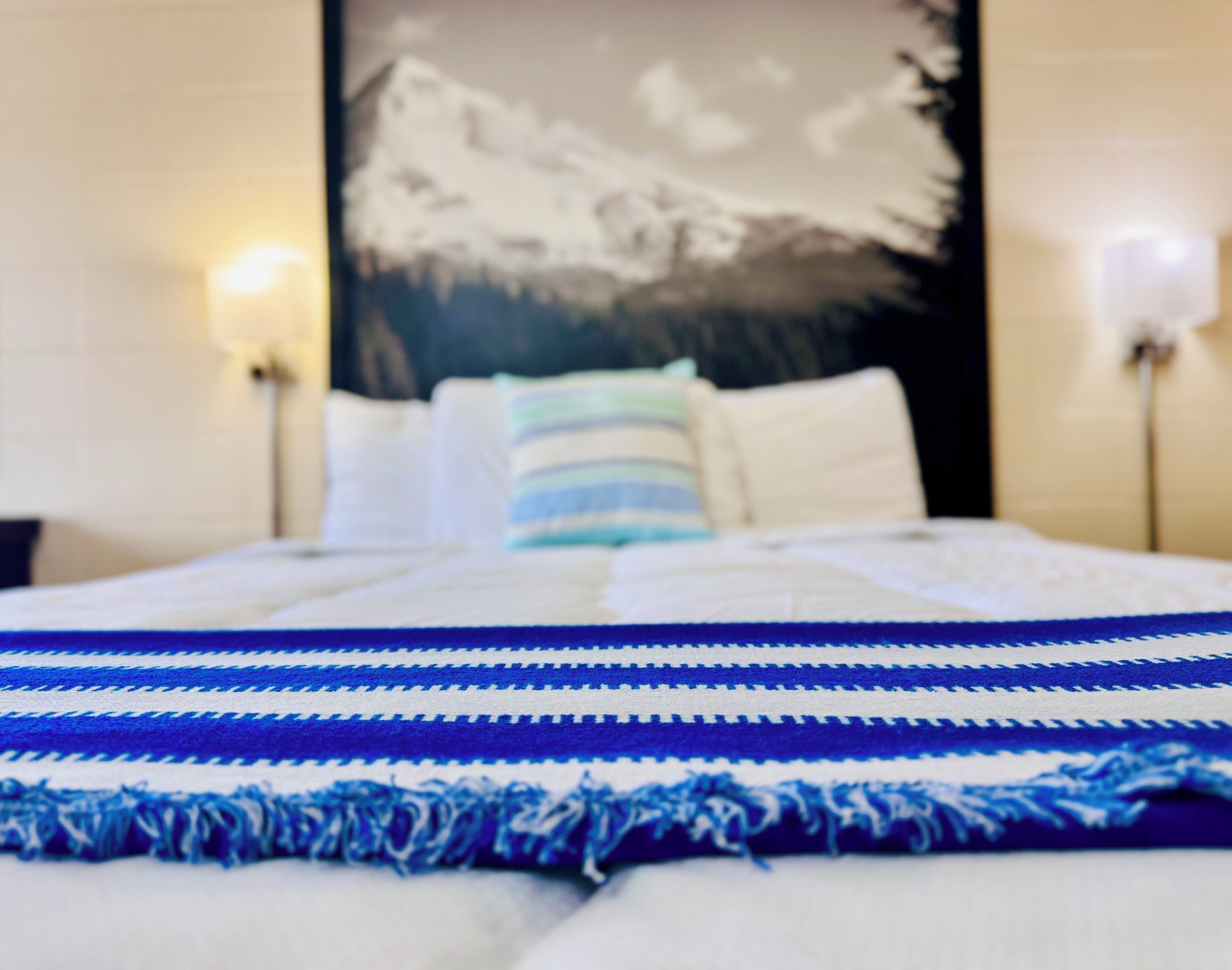 A bed with a blue and white striped blanket, white pillows, and a wall-mounted lamp.