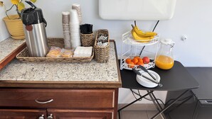 A breakfast setup with a stainless steel water bottle, stacked plates, and baskets containing bread, utensils, and fruits like bananas, oranges, and apples. - Relax Inn At Ashland (Ashland)
