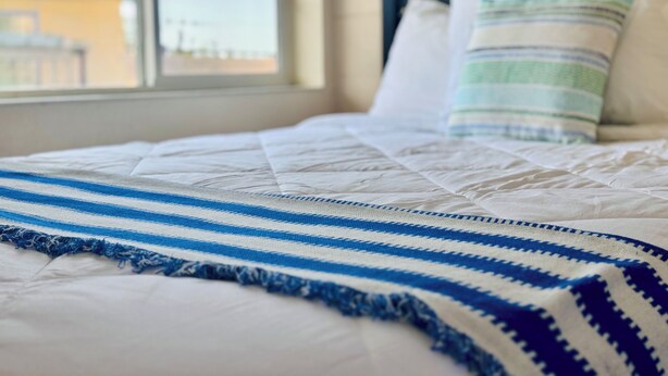 A bed with a striped blanket, a pillow, and a view of a cityscape through a window. - Relax Inn At Ashland (Ashland)