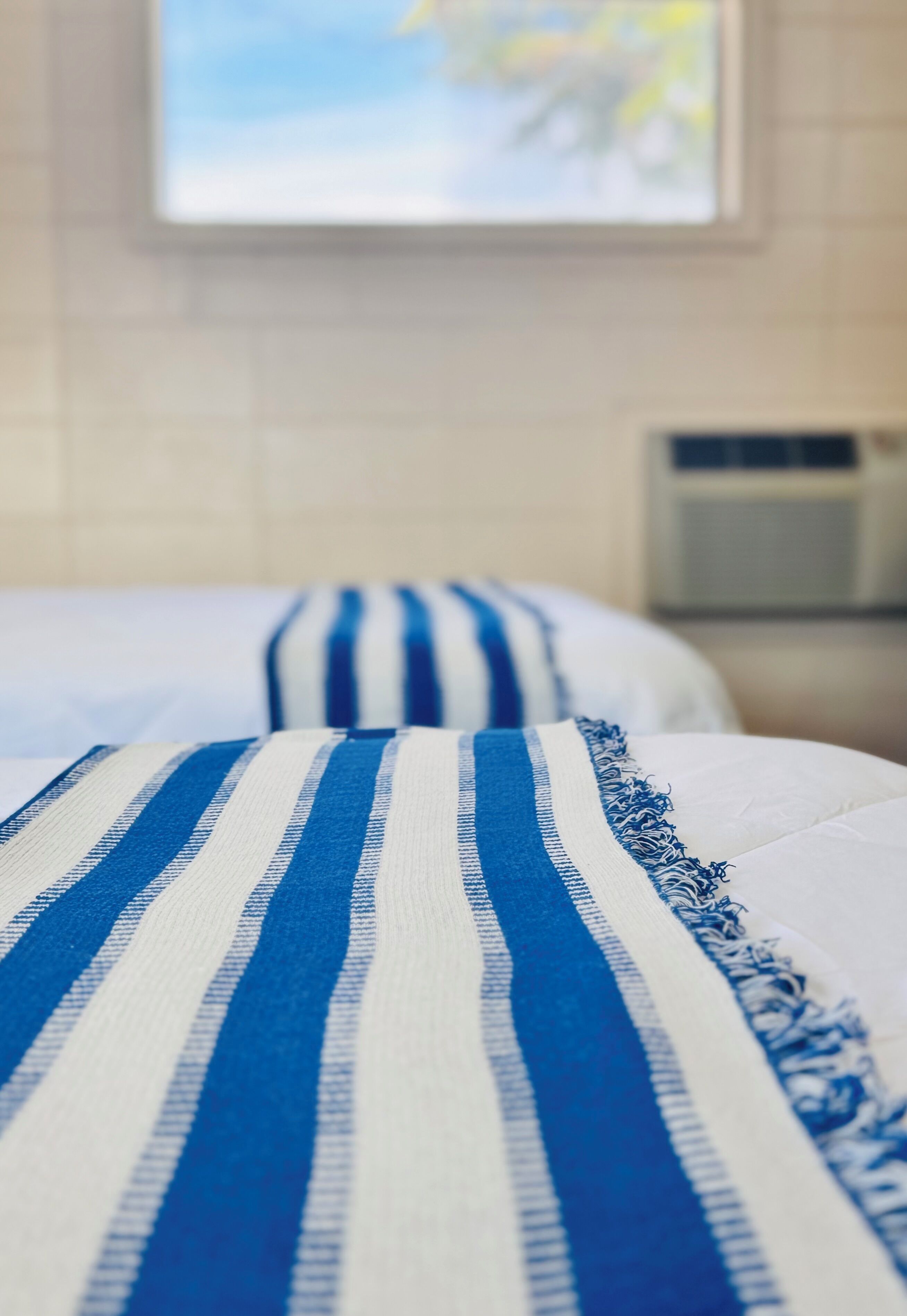 A hotel room with two beds, each with a striped bedspread.