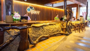 Zona de recepción con un mostrador de madera, un reloj y un cartel que dice 'Dusit Bunnuek Resort Koh Tao Thailand'.