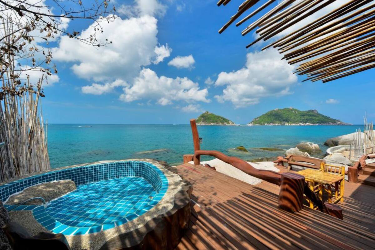 A wooden deck with a hot tub, lounge chairs, and a view of the sea and a small island.