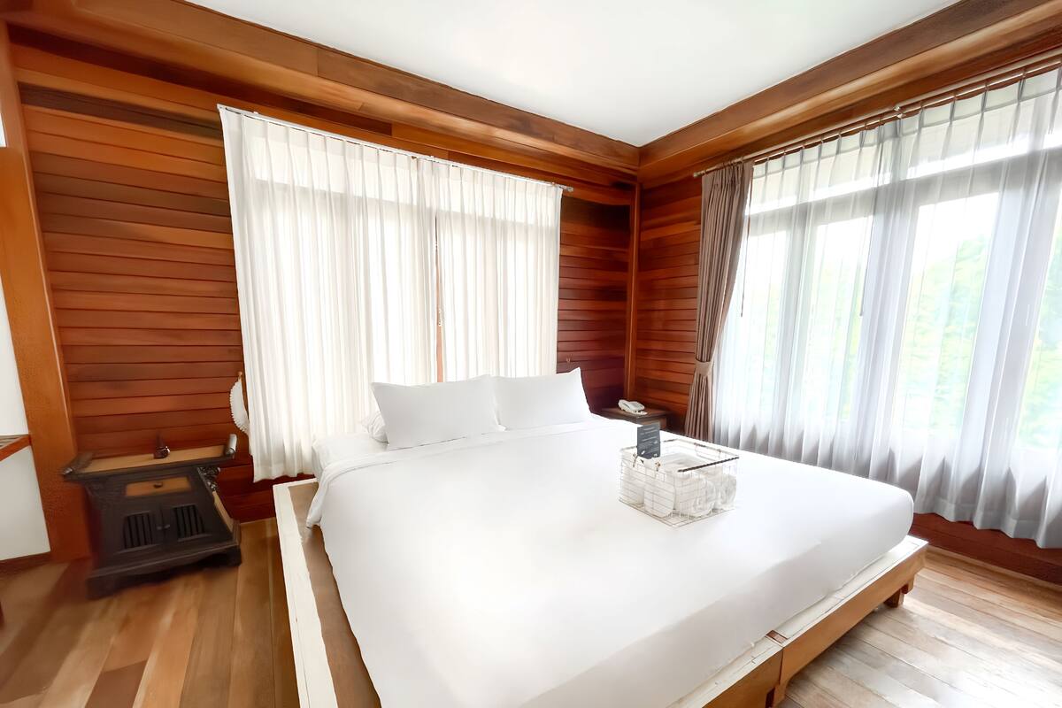 A large bed with white linens, wooden paneling on the walls, and a wooden floor.