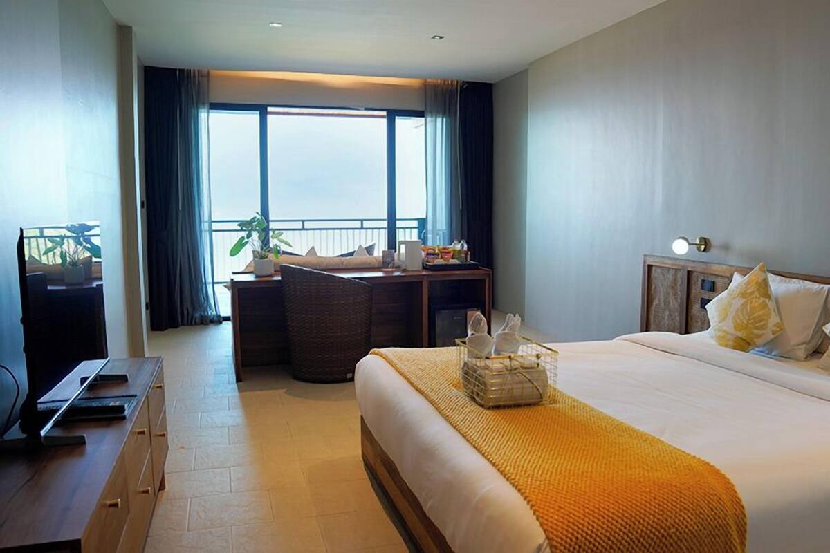 A hotel room with a large bed, a desk with a chair, a television, and a window with curtains.