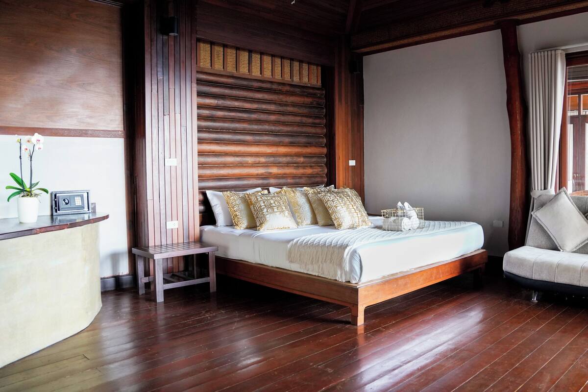 A bedroom with a wooden bed, a sofa, a small table, and a potted plant.