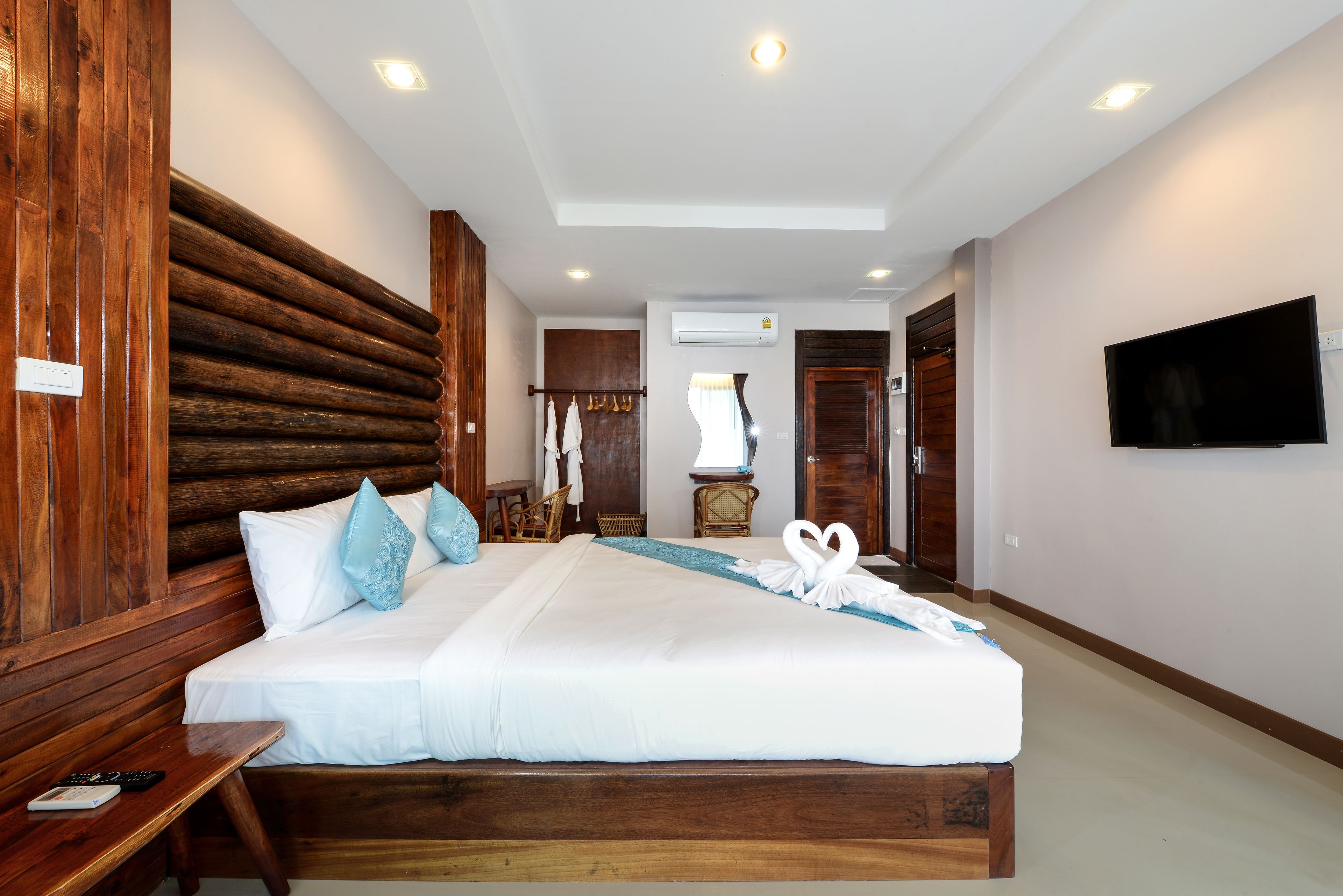 Camera d'albergo con un letto grande, una testiera in legno, una TV a schermo piatto e una panca di legno.