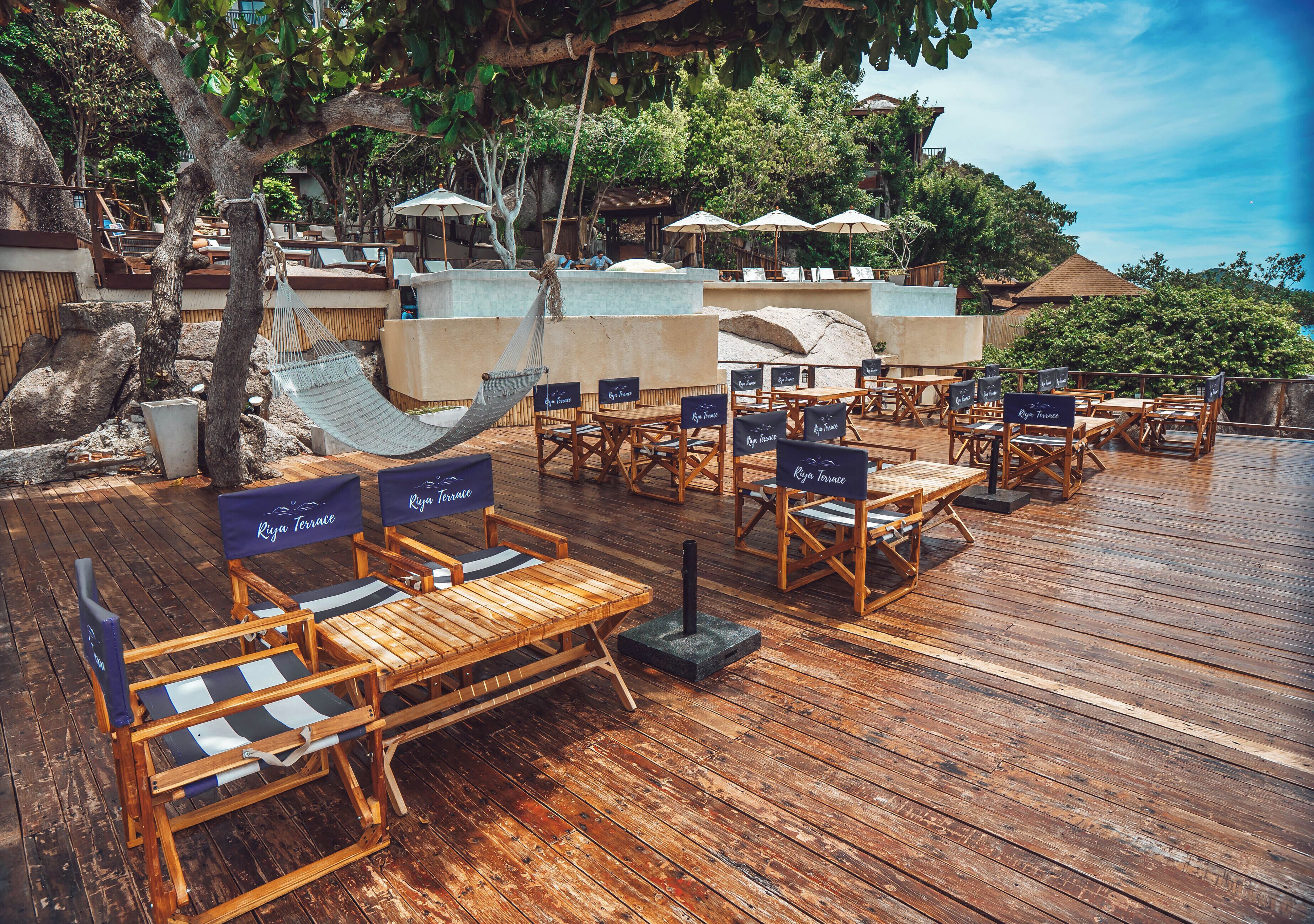 A wooden deck with lounge chairs and umbrellas, surrounded by trees and a view of a hill.