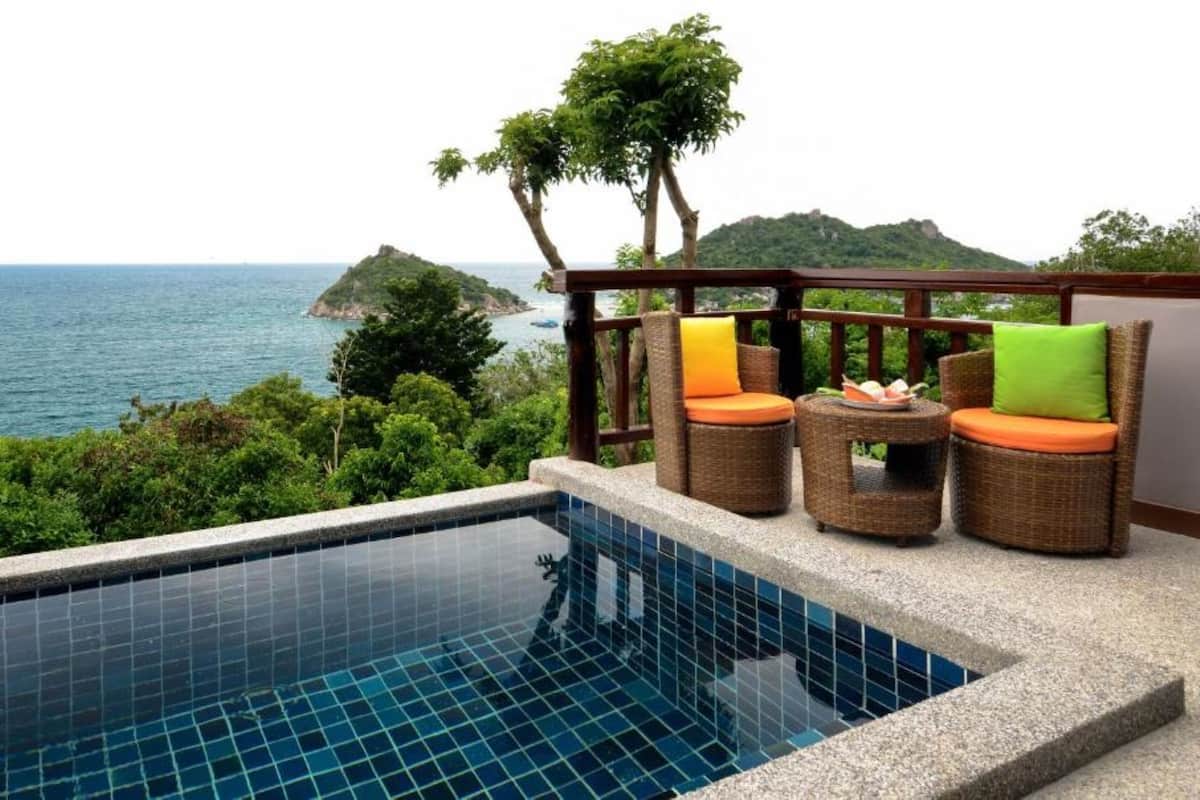 A poolside area with wicker furniture and a view of the sea.
