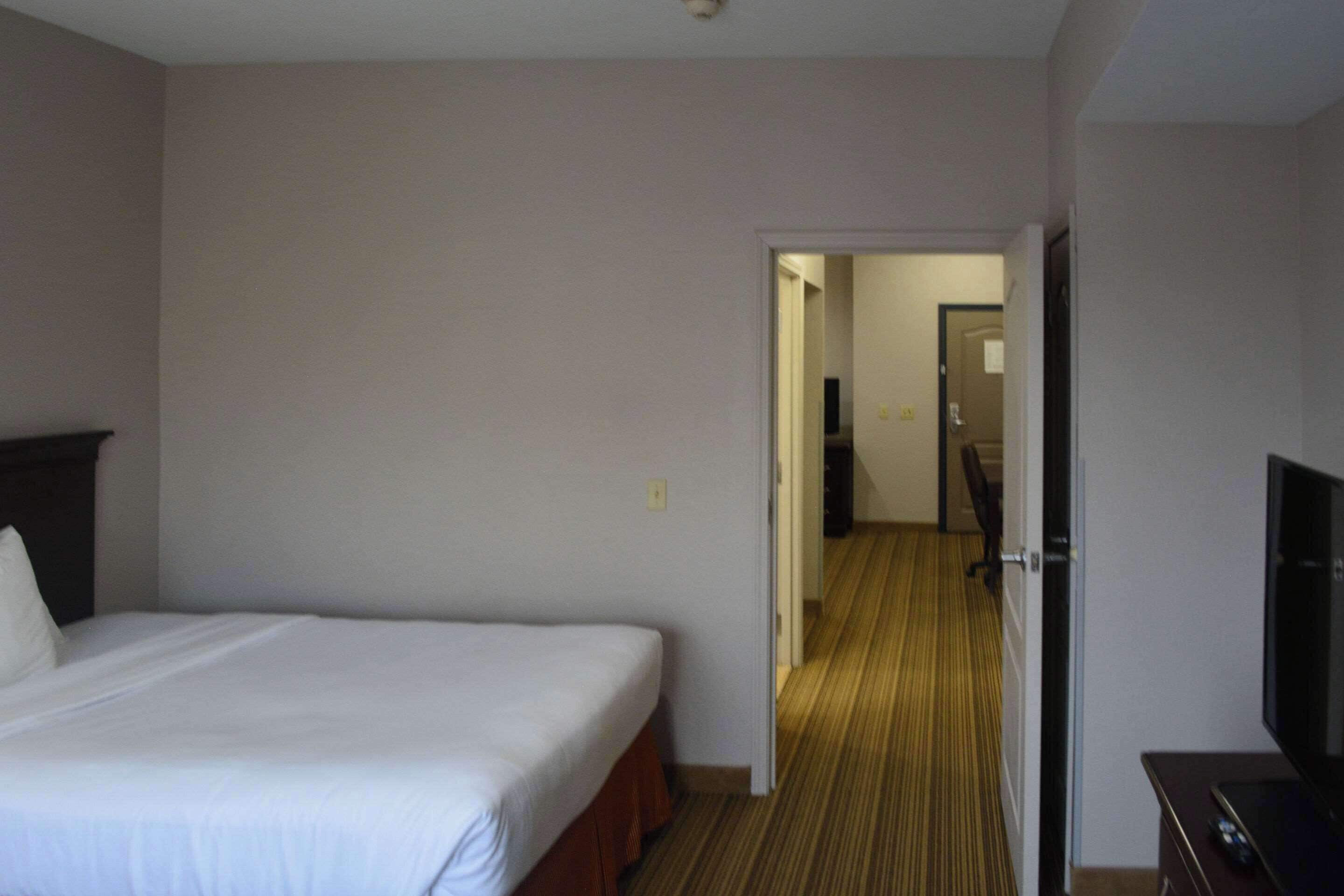 A hotel room with a single bed, a television on a stand, and a door leading to a hallway.
