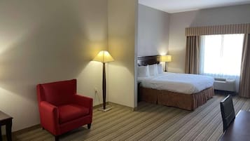 Une chambre d’hôtel avec un lit, un fauteuil rouge, un bureau et une lampe.