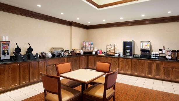 A hotel breakfast area with a wooden counter, seating, and various breakfast items. - Country Inn & Suites by Radisson, Oklahoma City - Quail Springs, OK (Oklahoma City)