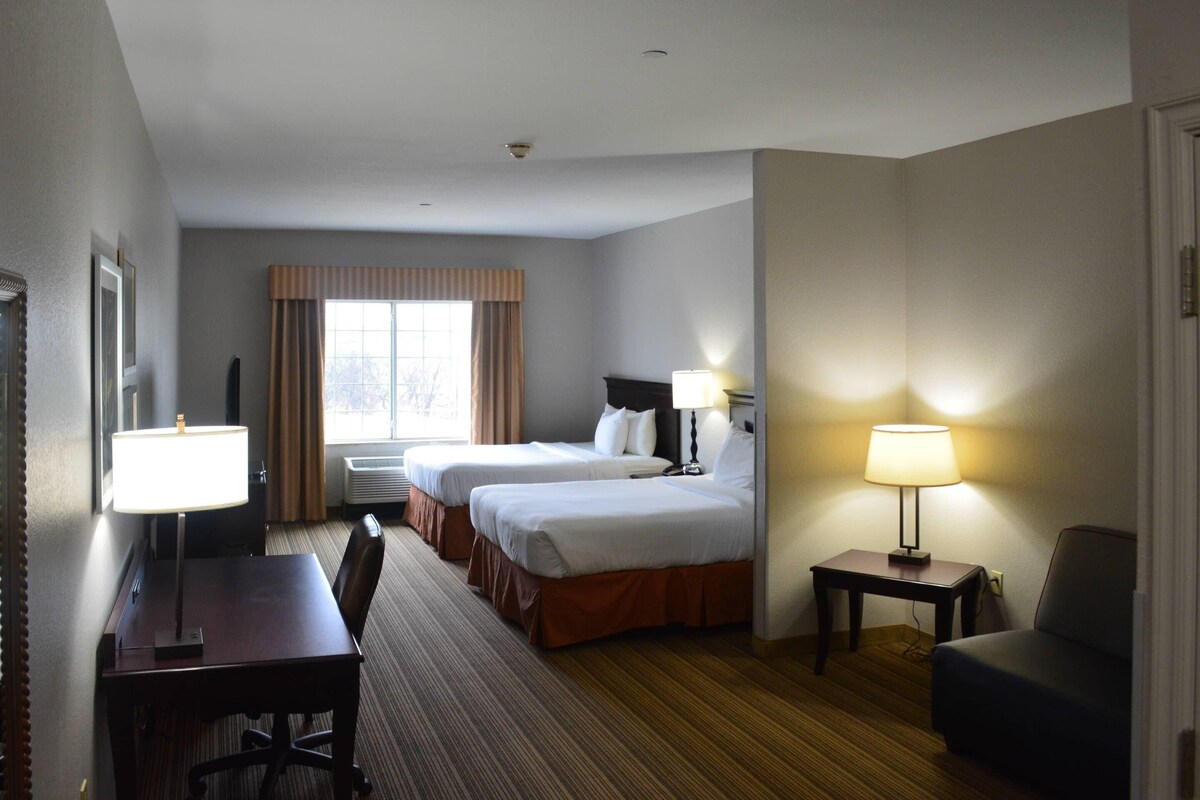 A hotel room with two beds, a desk, a chair, a lamp, and a window with curtains.