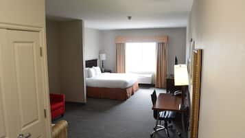 Habitación de hotel con cama, escritorio y silla, sillón rojo y un espejo grande.