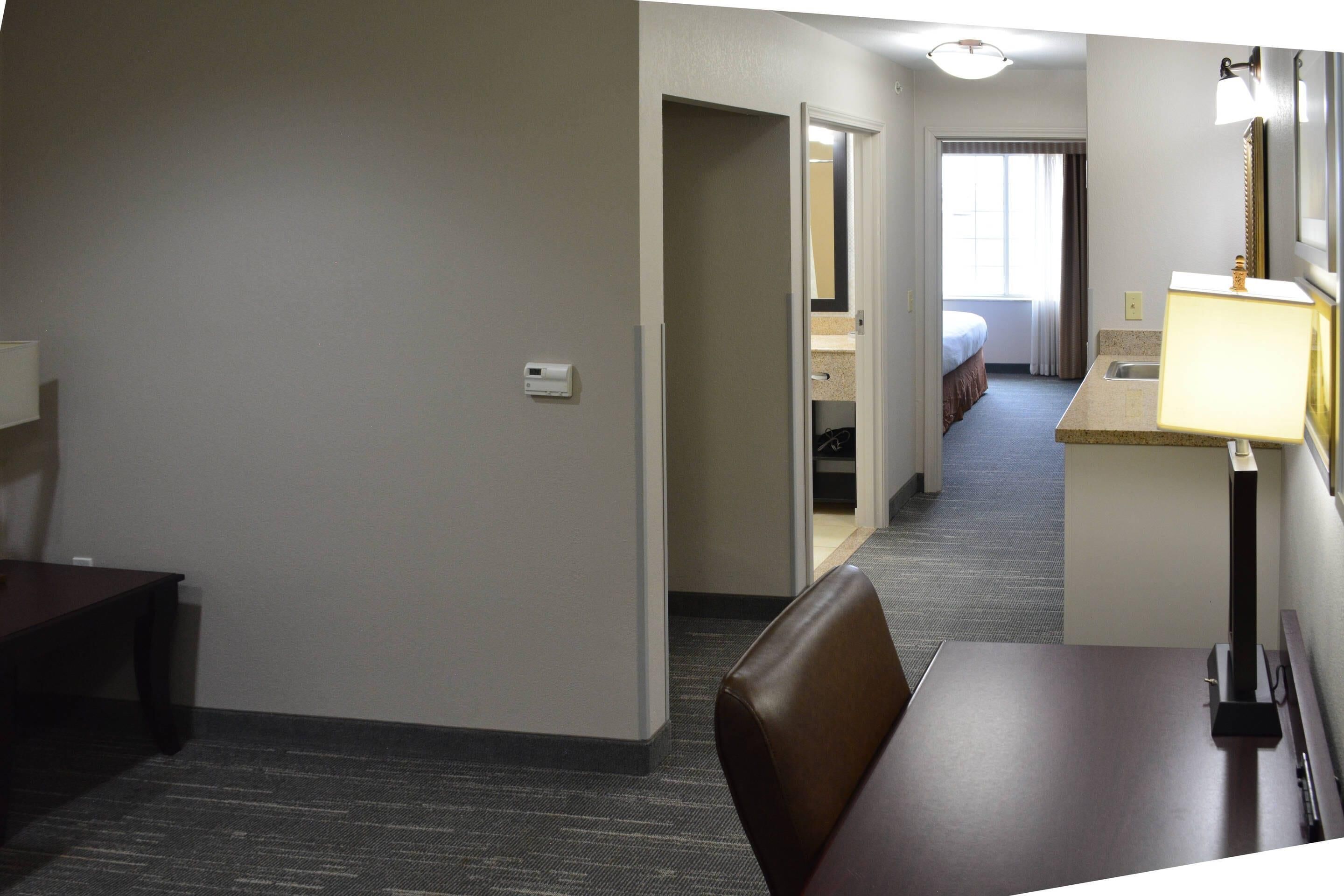 A hotel room with a bed, a desk, a chair, a lamp, and a bathroom visible through an open door.