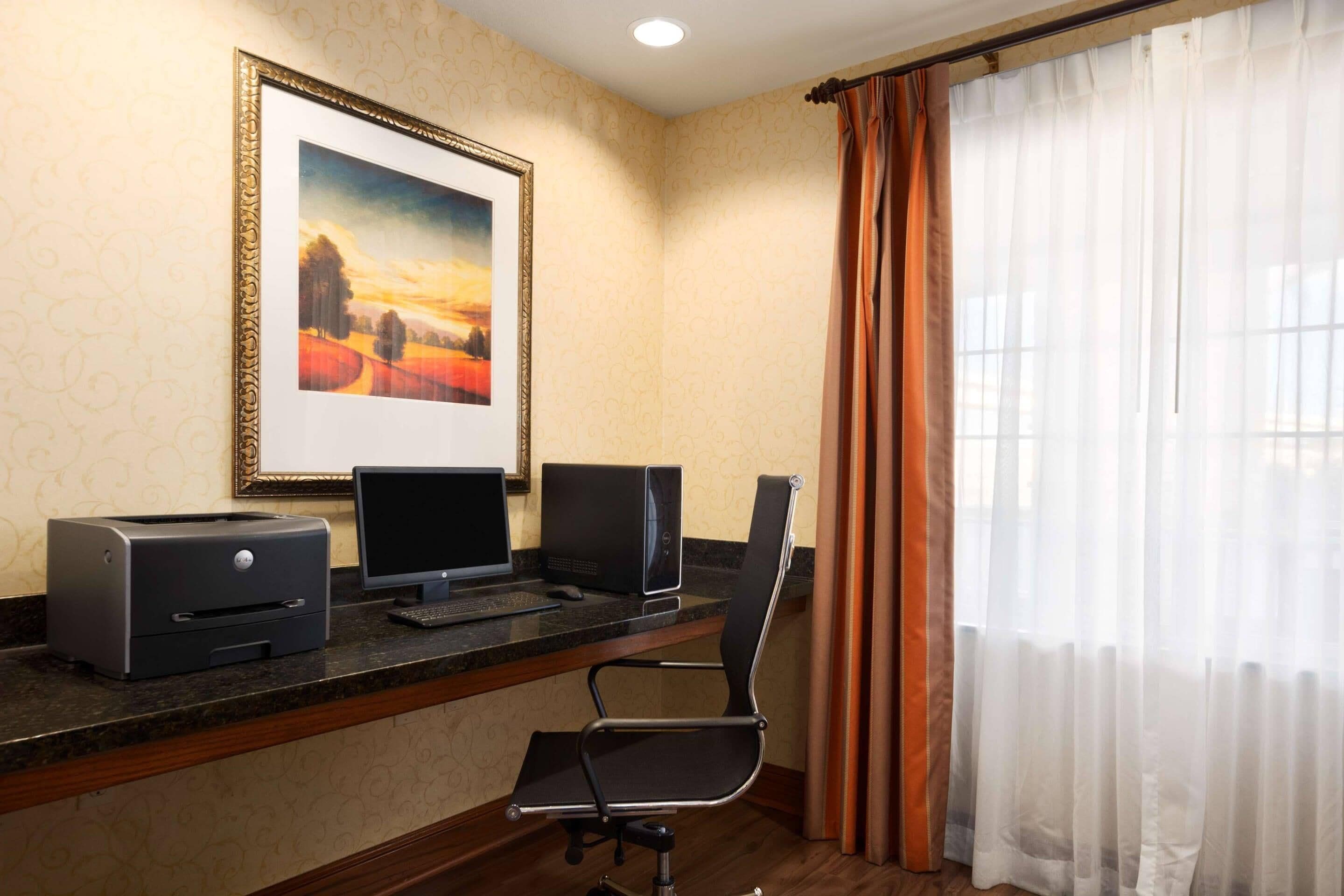 Habitación de hotel con un escritorio, dos monitores, una impresora y un cuadro en la pared.