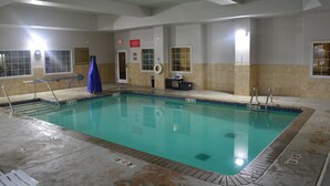 Una piscina interior con agua cristalina, paredes de azulejos y una silla para socorrista.