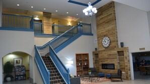 A spacious living area with a staircase, a fireplace, and a clock on the wall. - Country Inn & Suites by Radisson, Oklahoma City - Quail Springs, OK (Oklahoma City)