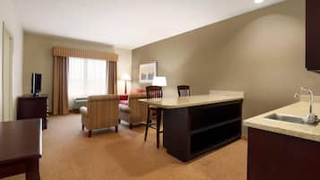 A compact hotel room with a kitchenette, a dining area, a sofa, and a television.