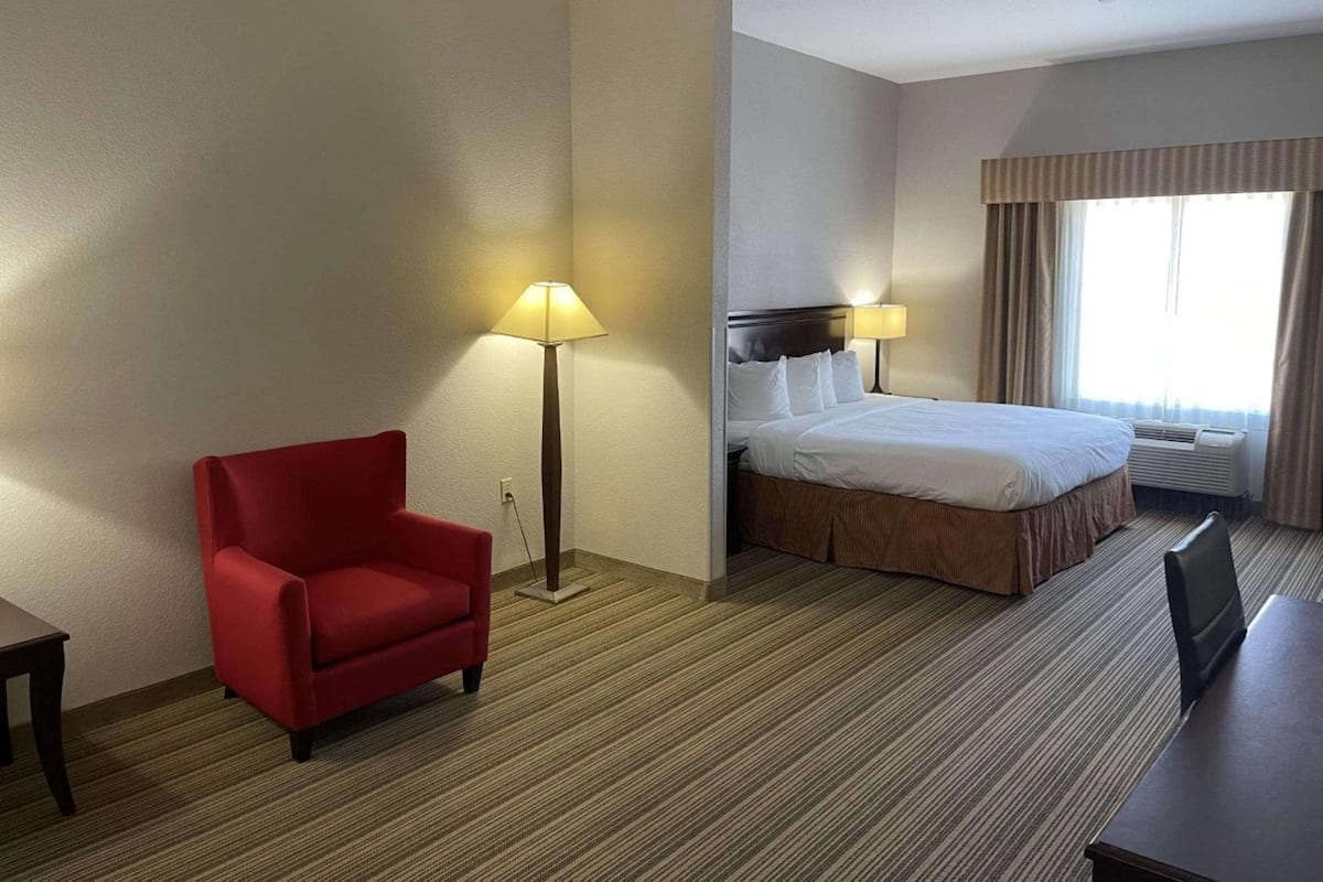 A hotel room with a bed, a red armchair, a desk, and a lamp.